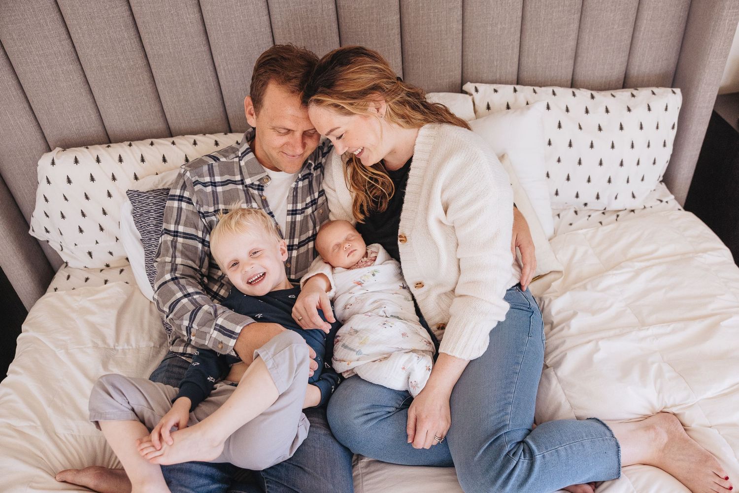 Cozy family moment captured on grey upholstered headboard bed with patterned pillows.