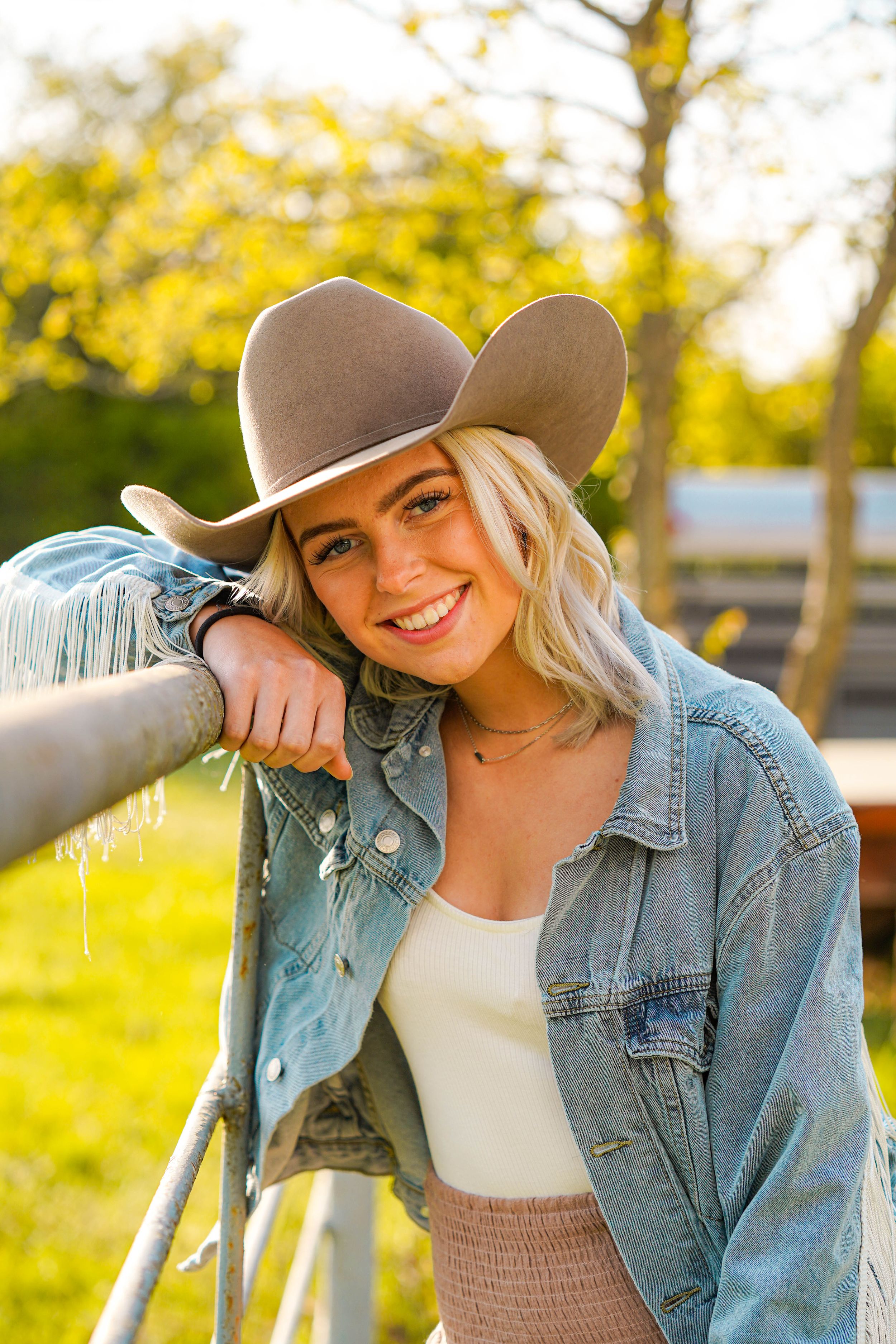 A person in a cowboy hat and denim jacket leans against a fence post in warm golden sunlight.