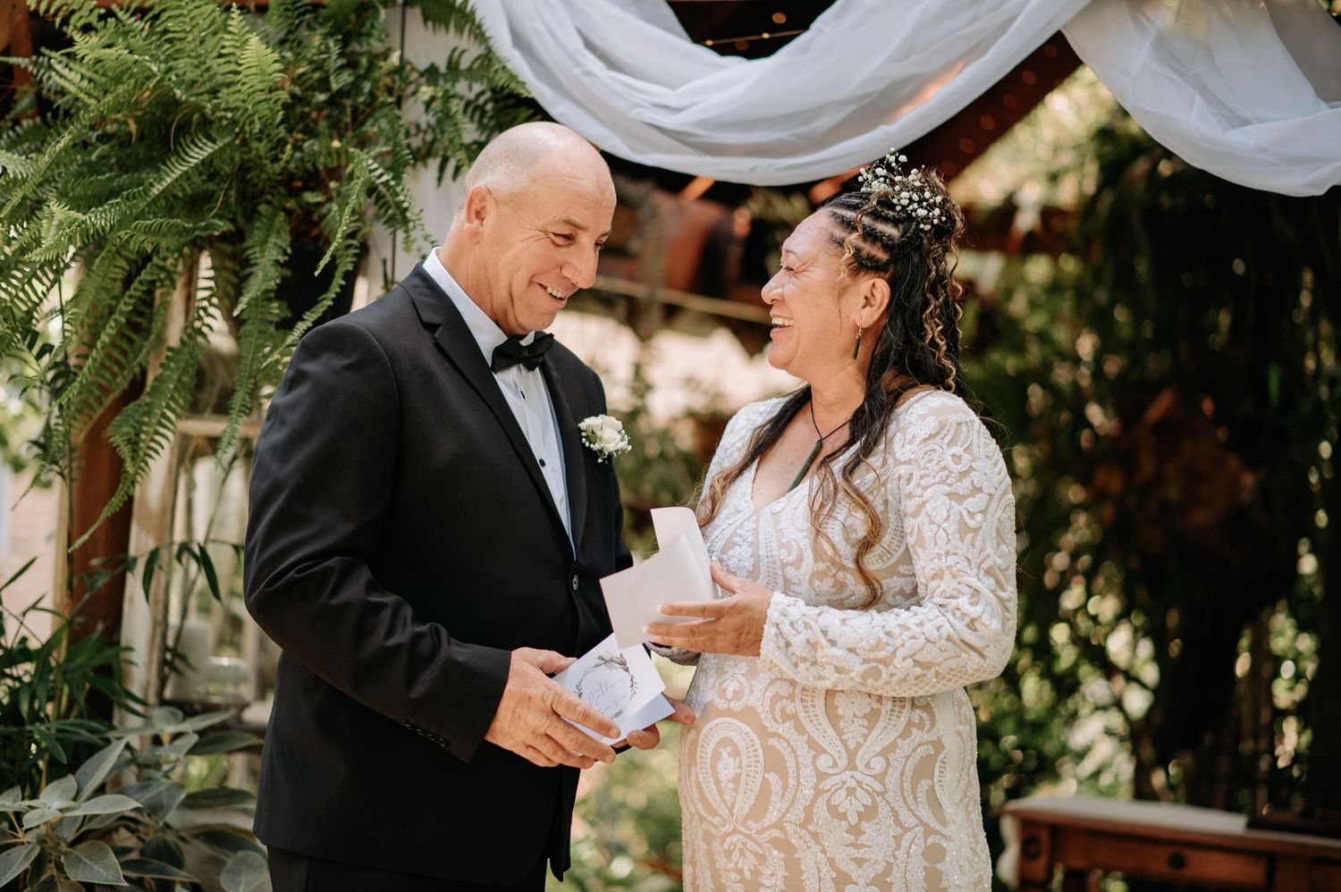 An emotional moment during a garden wedding ceremony with white drapery and greenery.