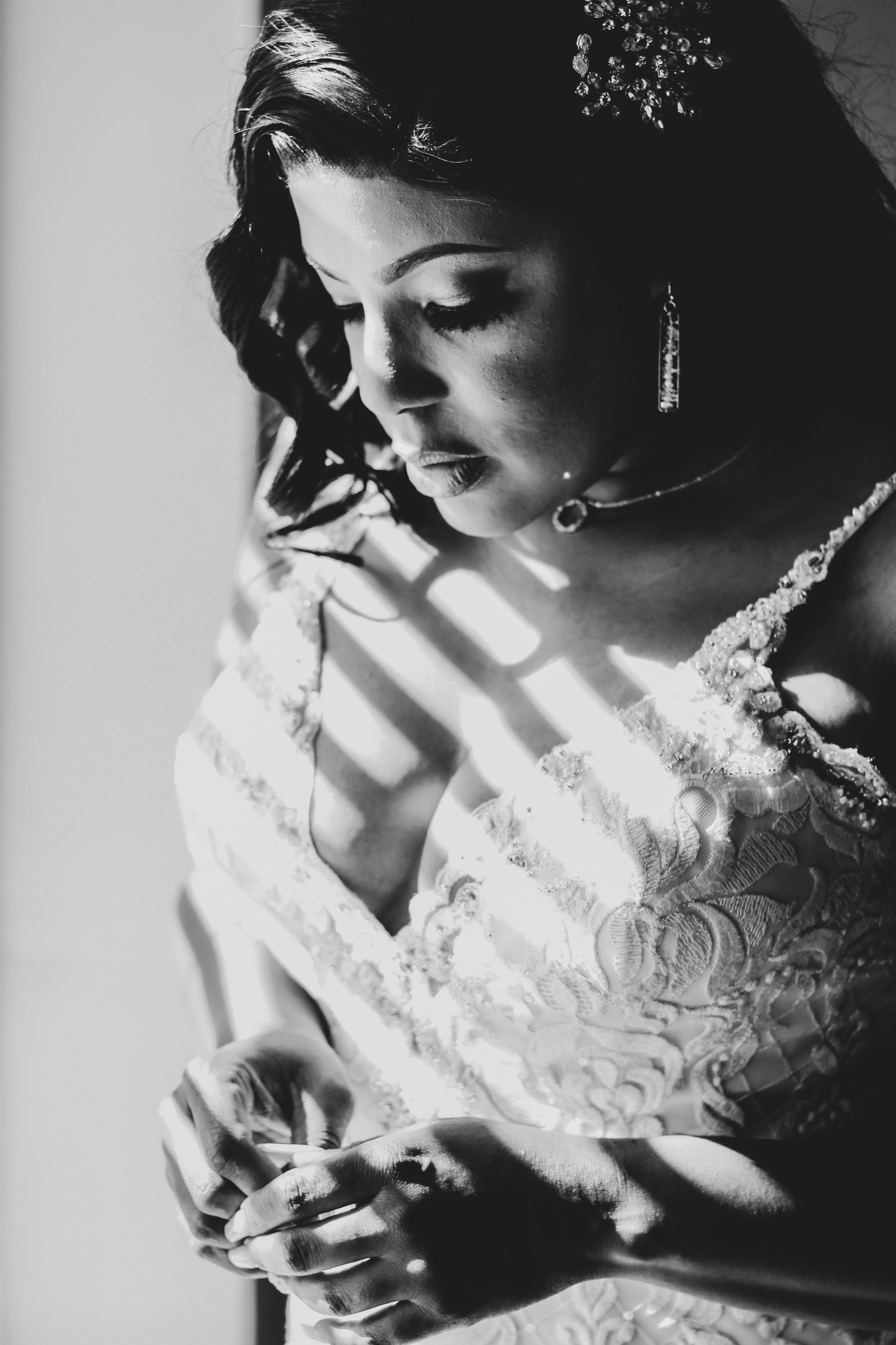 Dramatic black and white portrait of bride in lace gown with light streaming through window.