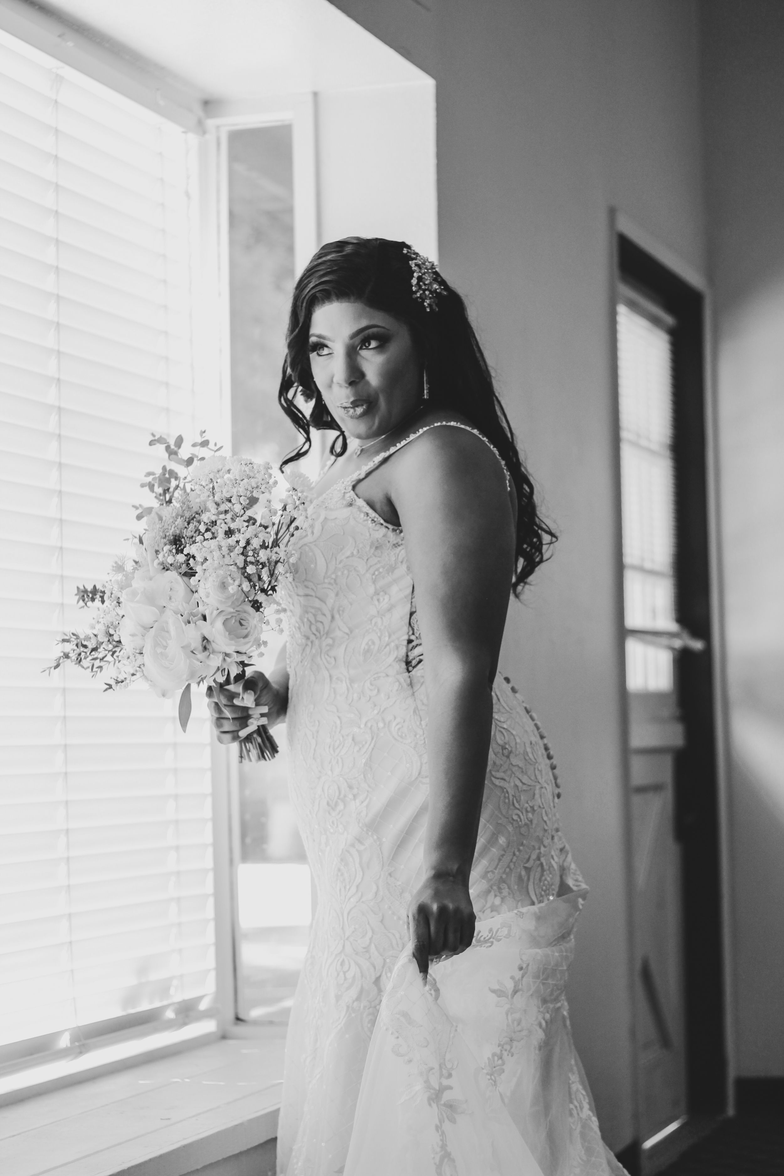 Black and white portrait of bride with bouquet near window.