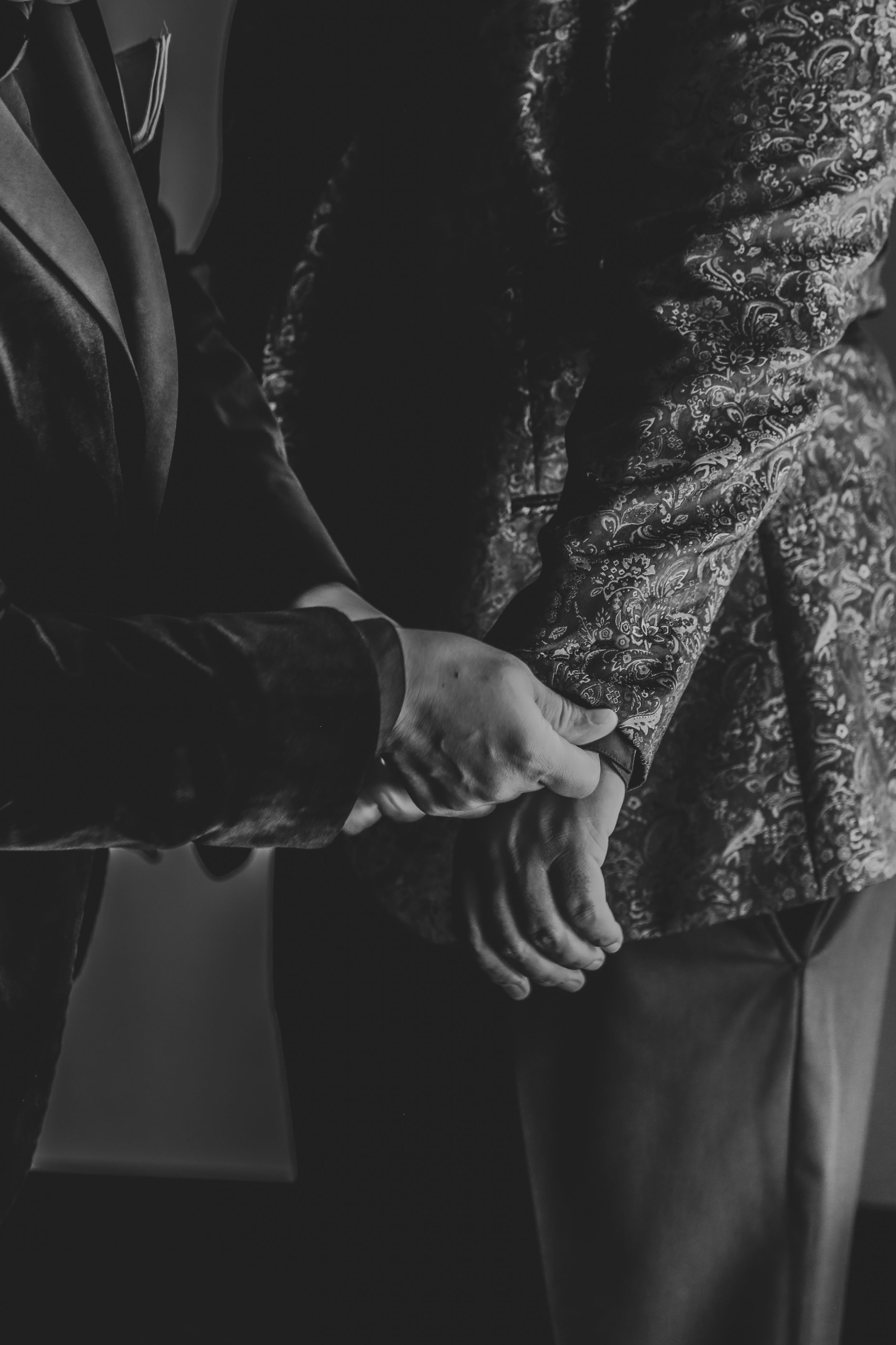 Close-up black and white photo of hands clasped together against formal attire.