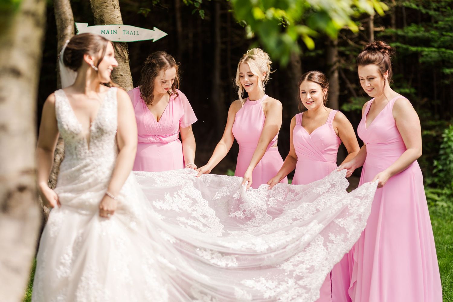 Bridesmaids in pink dresses help arrange the bride's lace wedding gown train.