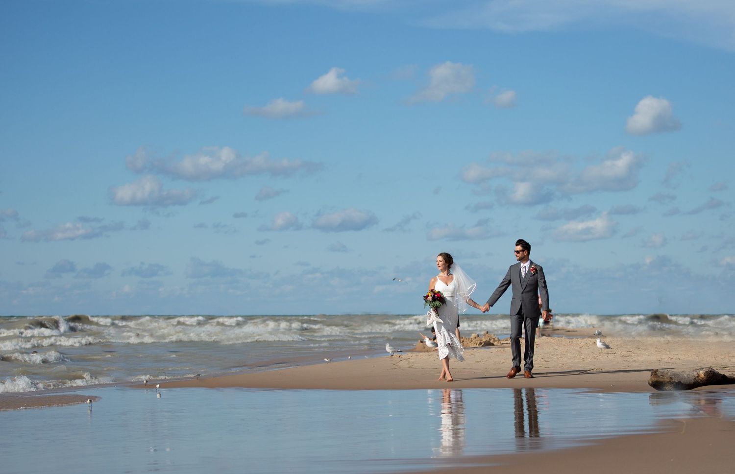Couple holding hands while walking along beach shoreline.