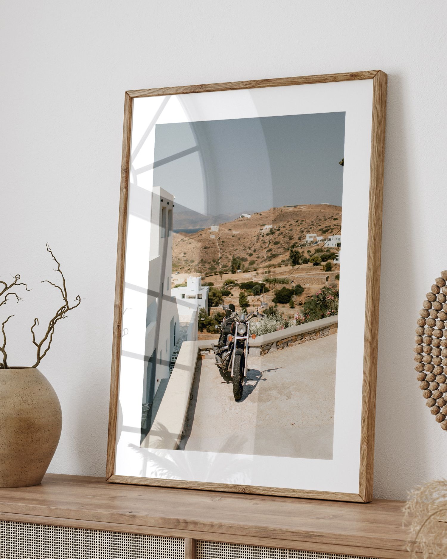 Framed photograph of scenic mountain road displayed on wooden console with decorative elements.