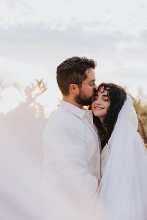 Intimate wedding portrait captured against a bright desert sky with soft lighting.