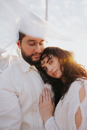 Intimate close-up of couple in white lace and cotton sharing tender moment in golden light.