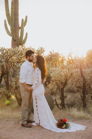 A couple shares a romantic moment at sunset in a desert landscape with saguaro cacti and cholla plants.