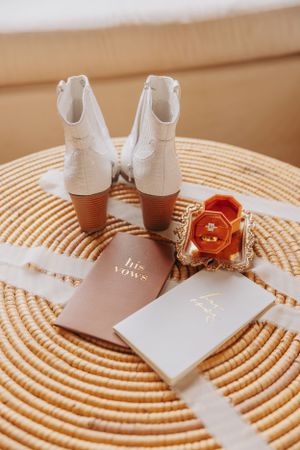 Wedding boots and vow books arranged on circular woven mat with gold accents.