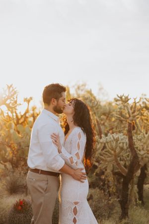 A tender moment between newlyweds in a desert setting with cacti and warm sunset light.