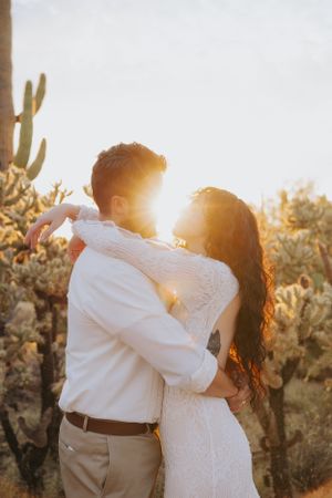 A loving embrace backlit by golden sunset light among desert cacti.