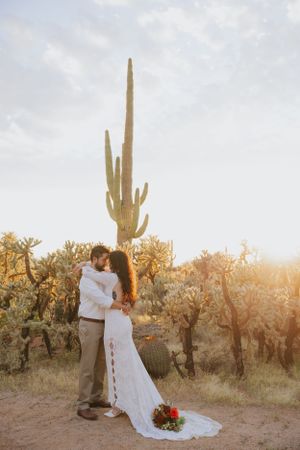 A romantic desert wedding portrait with saguaro cacti silhouetted against the setting sun.