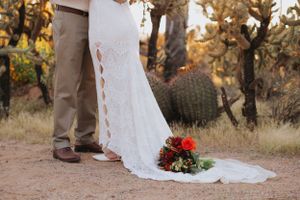 A desert wedding scene with a flowing white dress and red bouquet among towering cacti.