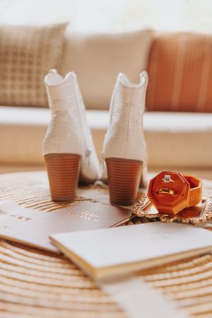 White leather boots and brown leather accessories arranged on a textured surface in warm lighting.