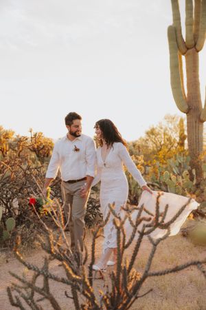 Candid desert engagement photos showing a couple walking through cacti during golden hour.