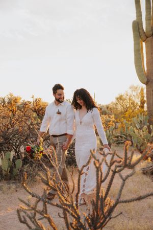 Couple in white and khaki outfits exploring a desert landscape with towering saguaro cacti.