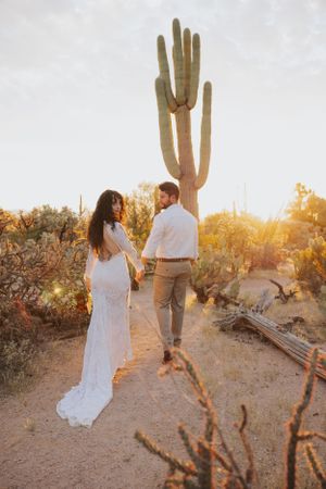 Desert engagement photography featuring a couple walking among cacti during sunset.