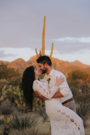 Romantic couple shares intimate moments against a desert landscape with saguaro cacti and mountains at sunset.
