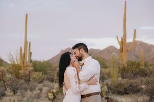 Desert engagement photos featuring a couple among saguaro cacti and desert brush at dusk.
