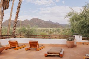 Outdoor patio with wooden lounge chairs overlooking desert mountains and palm trees.