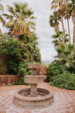 Circular stone fountain surrounded by palm trees and desert landscaping on a tiled patio.