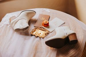 Wedding details including white boots and gold accessories on circular wooden surface.