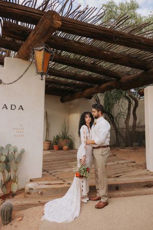 Couple poses against white adobe wall with rustic wooden beams and desert plants at ADA venue.