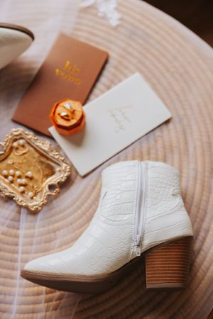 White leather wedding boots next to vow books and gold decorative elements.