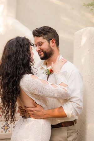 Romantic desert wedding photos with couple in white dress and casual attire against adobe walls.