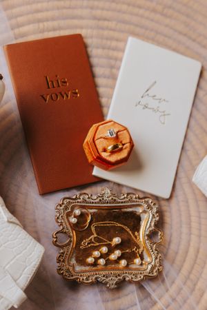 Wedding vow books with gold wax seals and ornate trays arranged on wooden table.