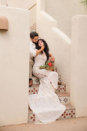 Wedding couple poses on southwestern tiled steps with desert landscaping and white walls.