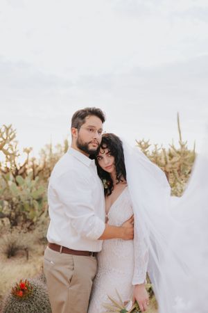 Desert wedding photos with couple embracing among cacti in white dress and khaki attire.