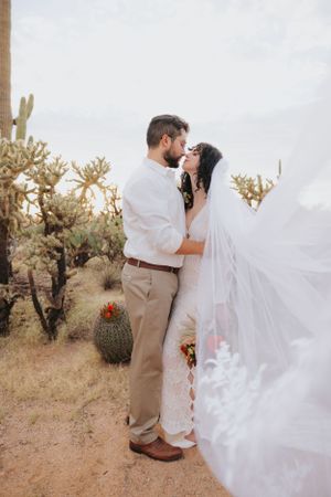 A romantic desert wedding photoshoot with a couple embracing among saguaro cacti and desert flora.
