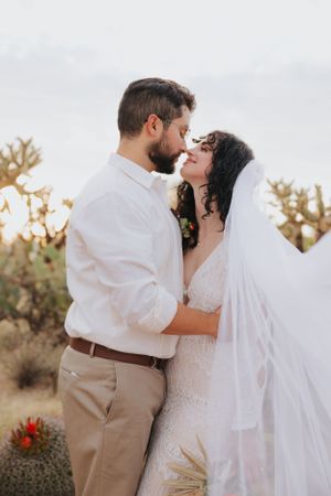 Newlyweds share an intimate moment in a desert landscape with cacti and soft lighting.