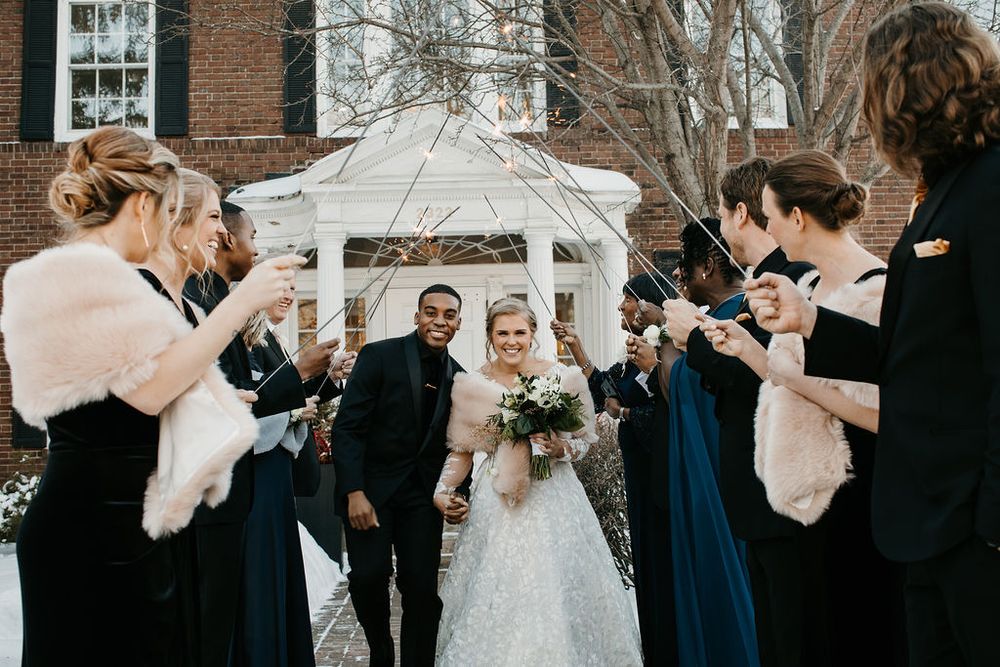 Bride and groom exit winter wedding venue through sparkler send-off with bridal party.
