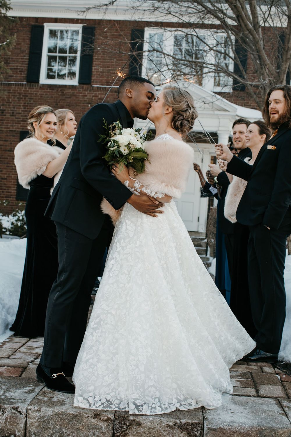 Newlywed couple shares romantic kiss during outdoor winter wedding sparkler send-off.