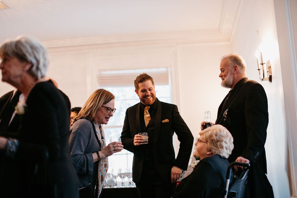 Wedding guests socializing and laughing together in a elegantly decorated white reception venue.