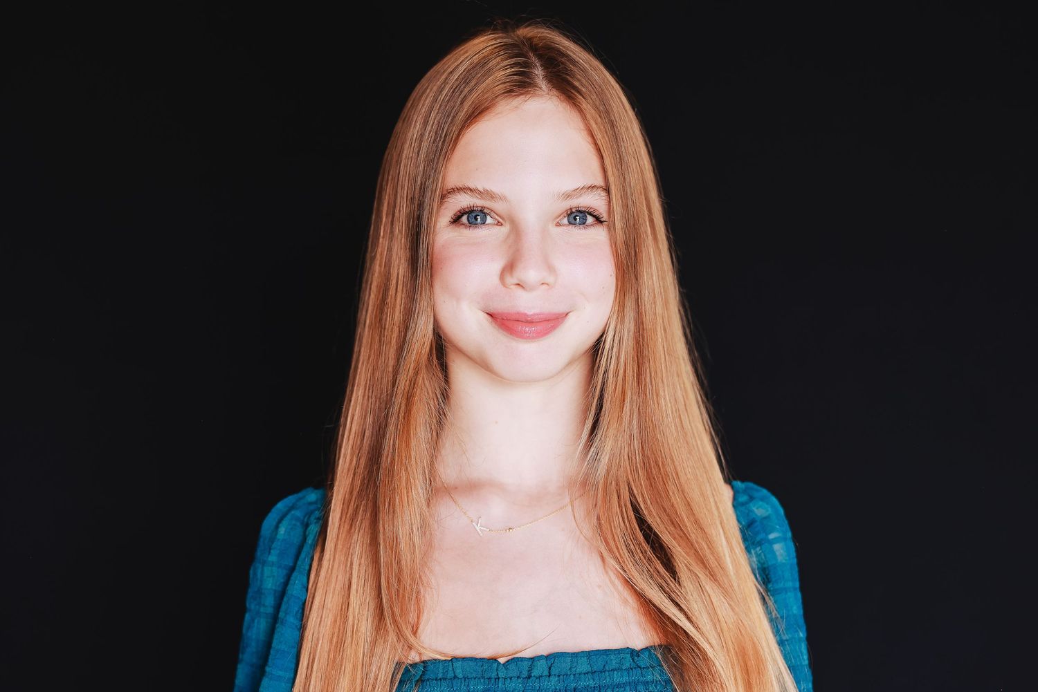 Portrait showing bright smile and long straight hair against dark background.