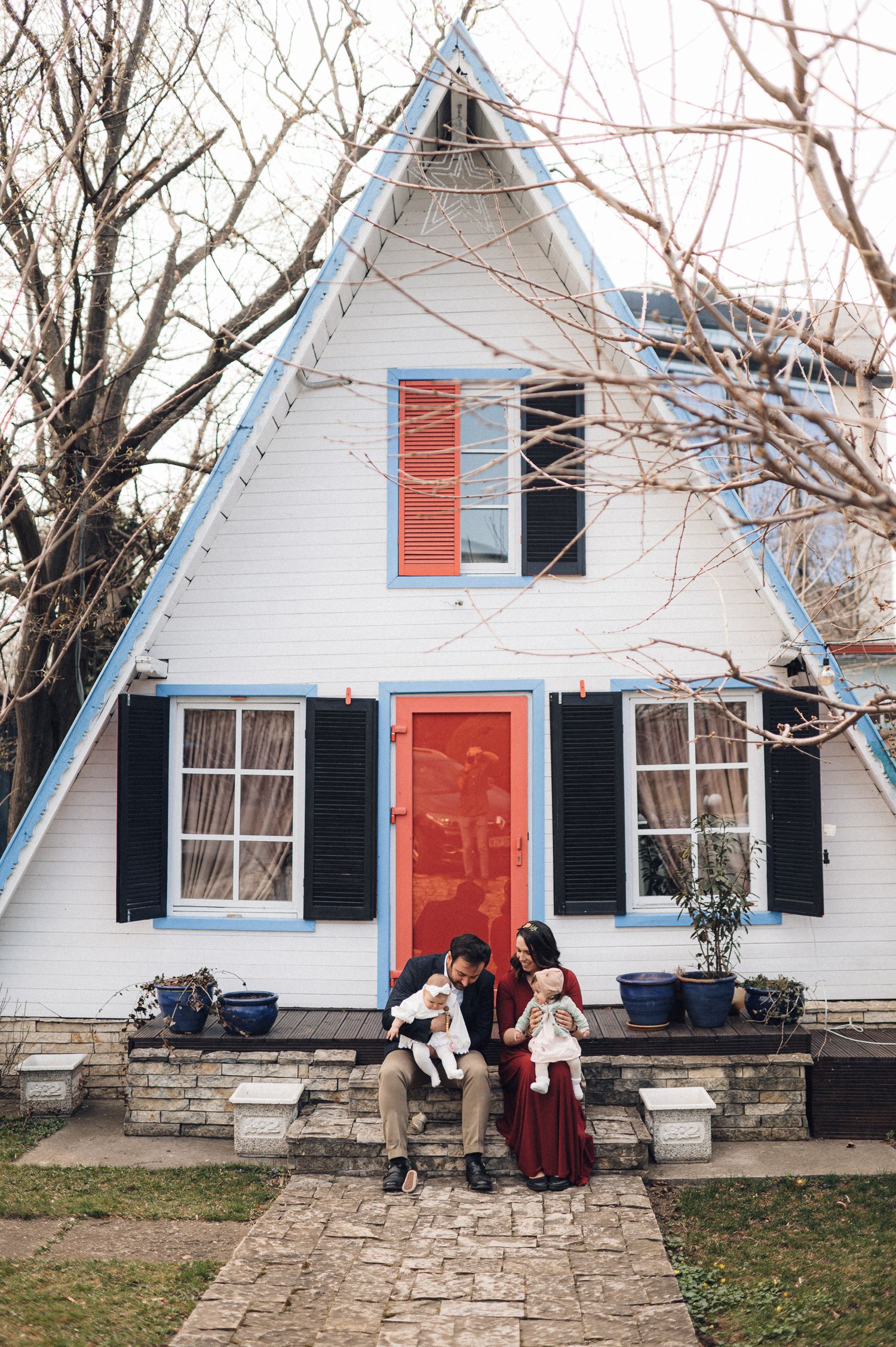 A-frame white house with blue trim and red door featuring people gathered on the front steps.