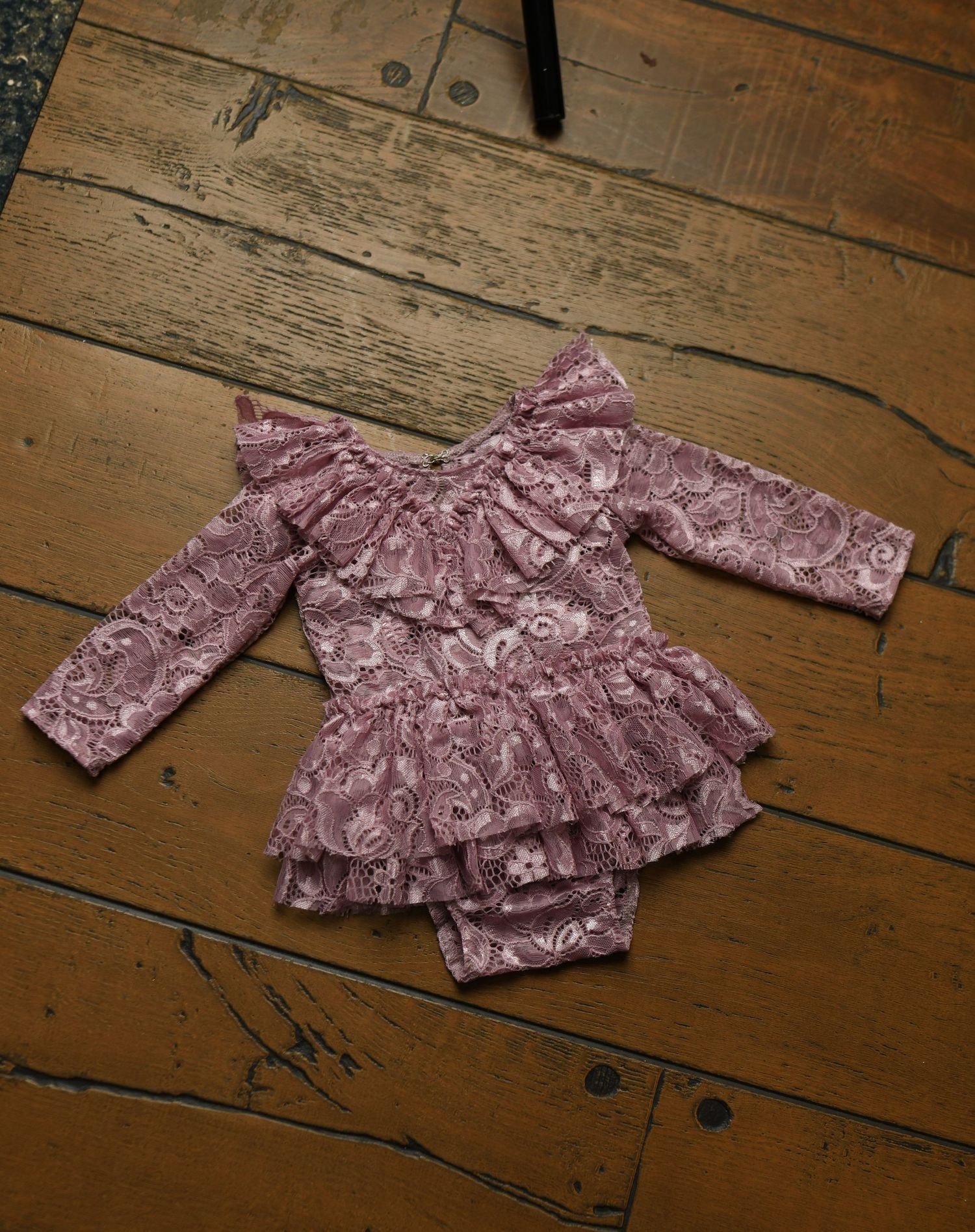 Dusty rose floral baby outfit with ruffled details on wooden background.