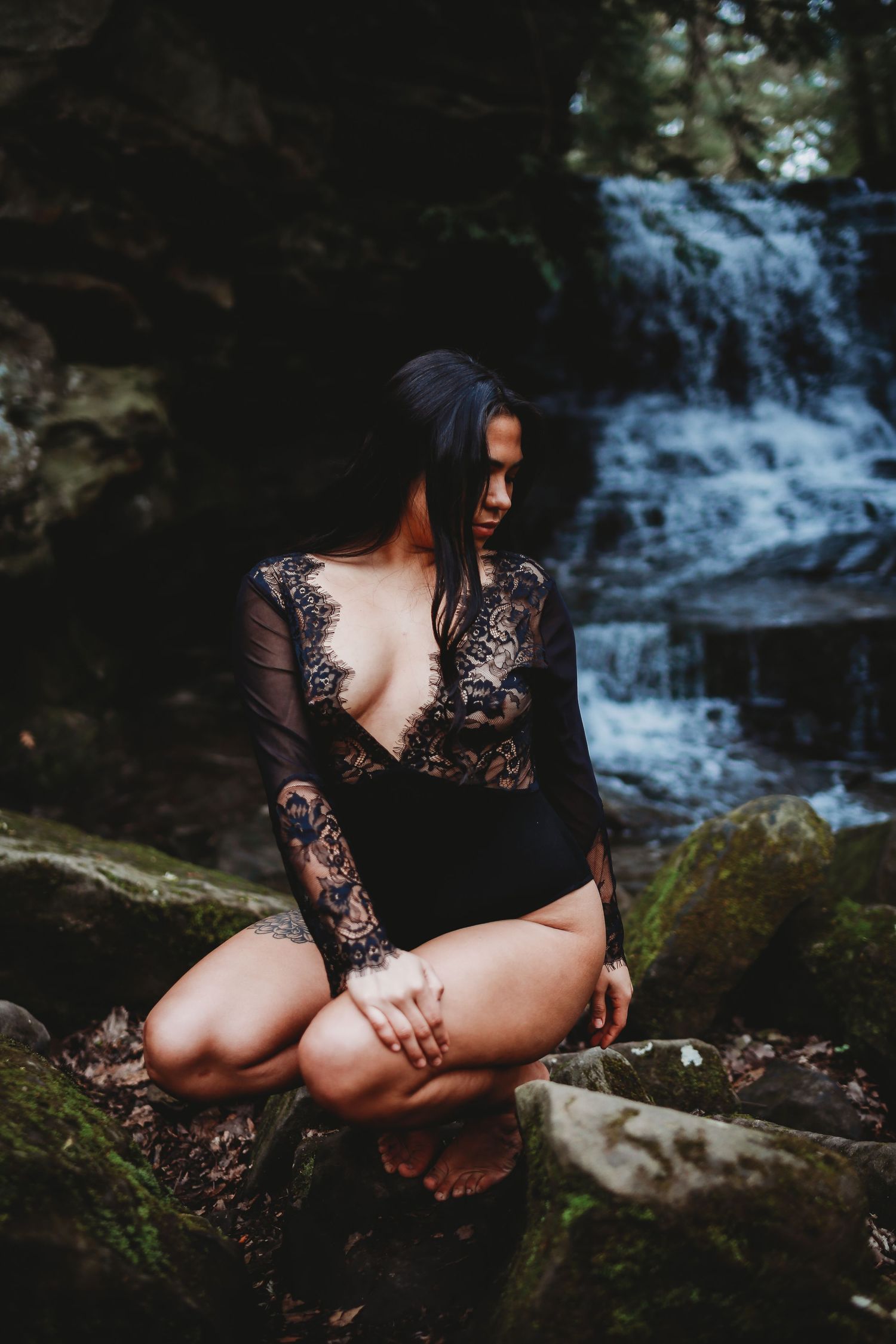 Artistic portrait by waterfall featuring black lace dress against natural rock backdrop.