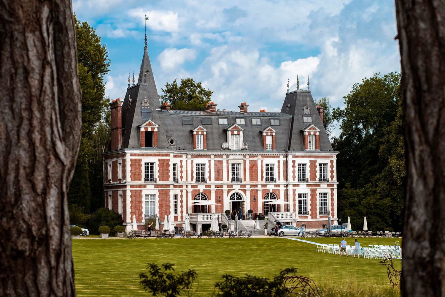 Elegant French-style chateau with red brick facades and ornate grey rooftops stands on manicured grounds.