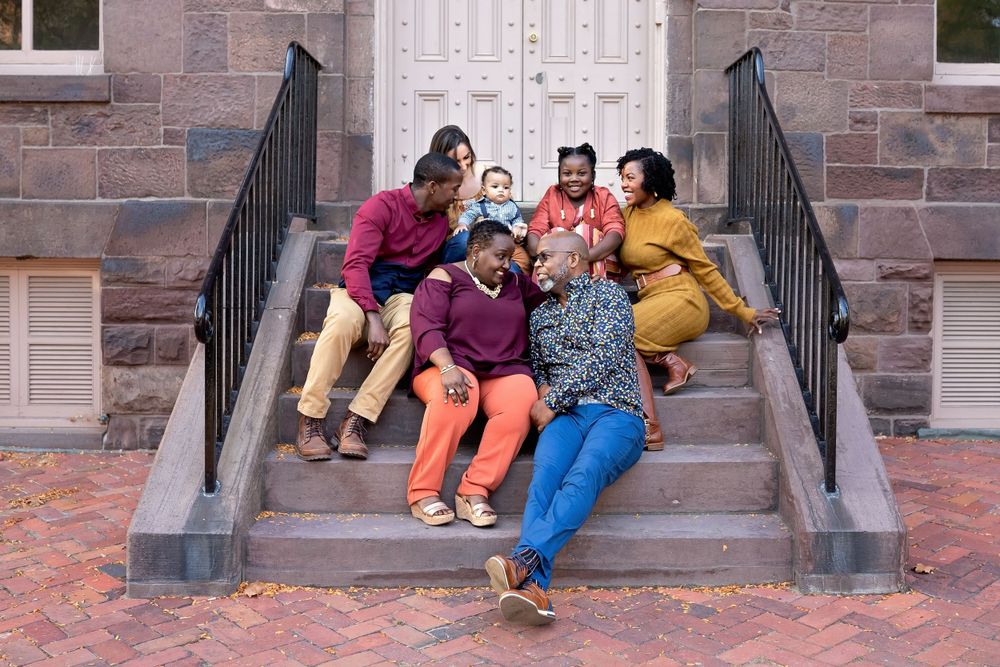 Joyful family of six laughs together on brick building steps during fall photo session.