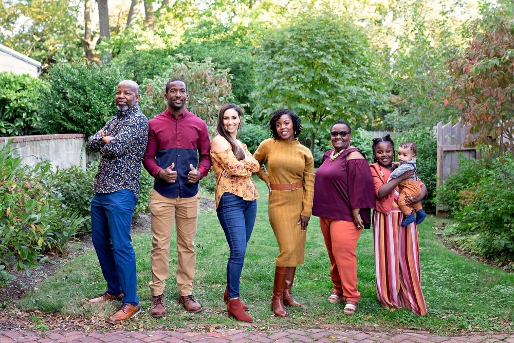Group of six adults smiling together in a lush garden setting.