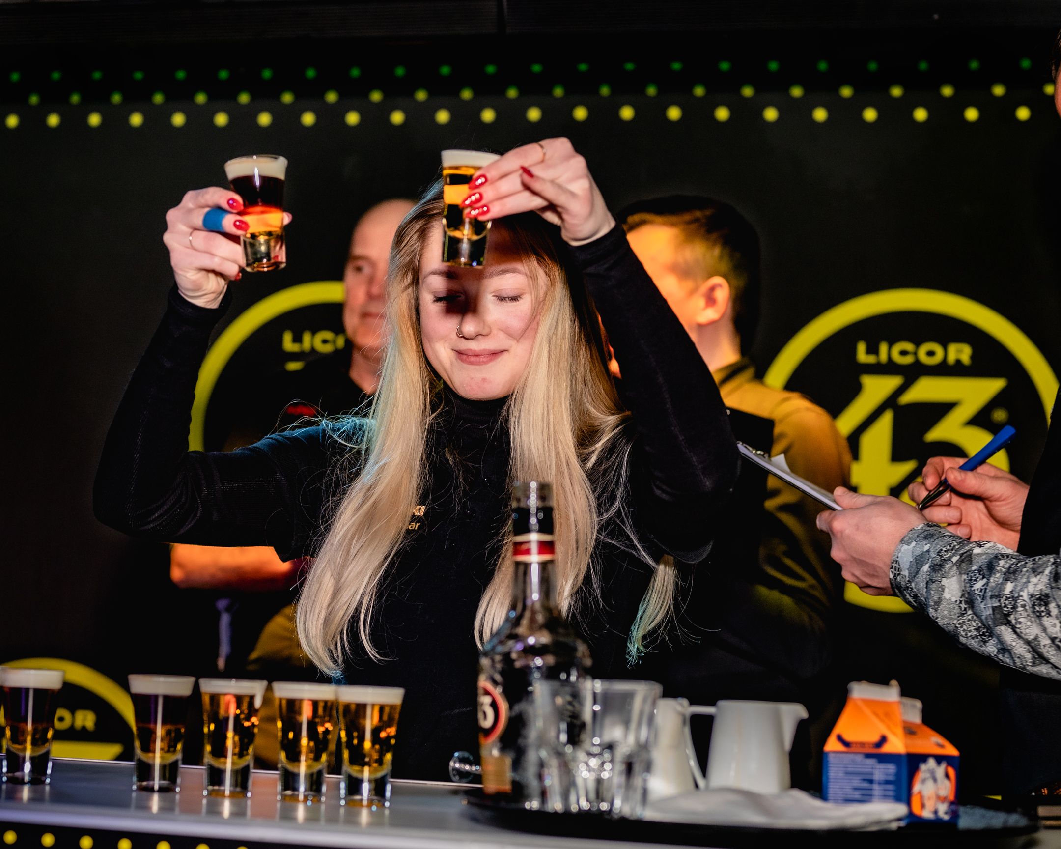 Bartender demonstration with multiple spirit bottles at a branded Licor 43 event.