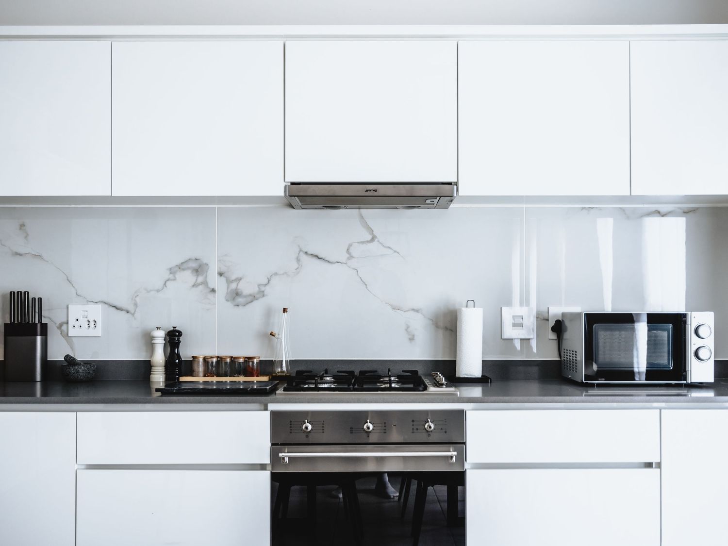 Contemporary white kitchen with marble backsplash featuring stovetop and modern appliances.