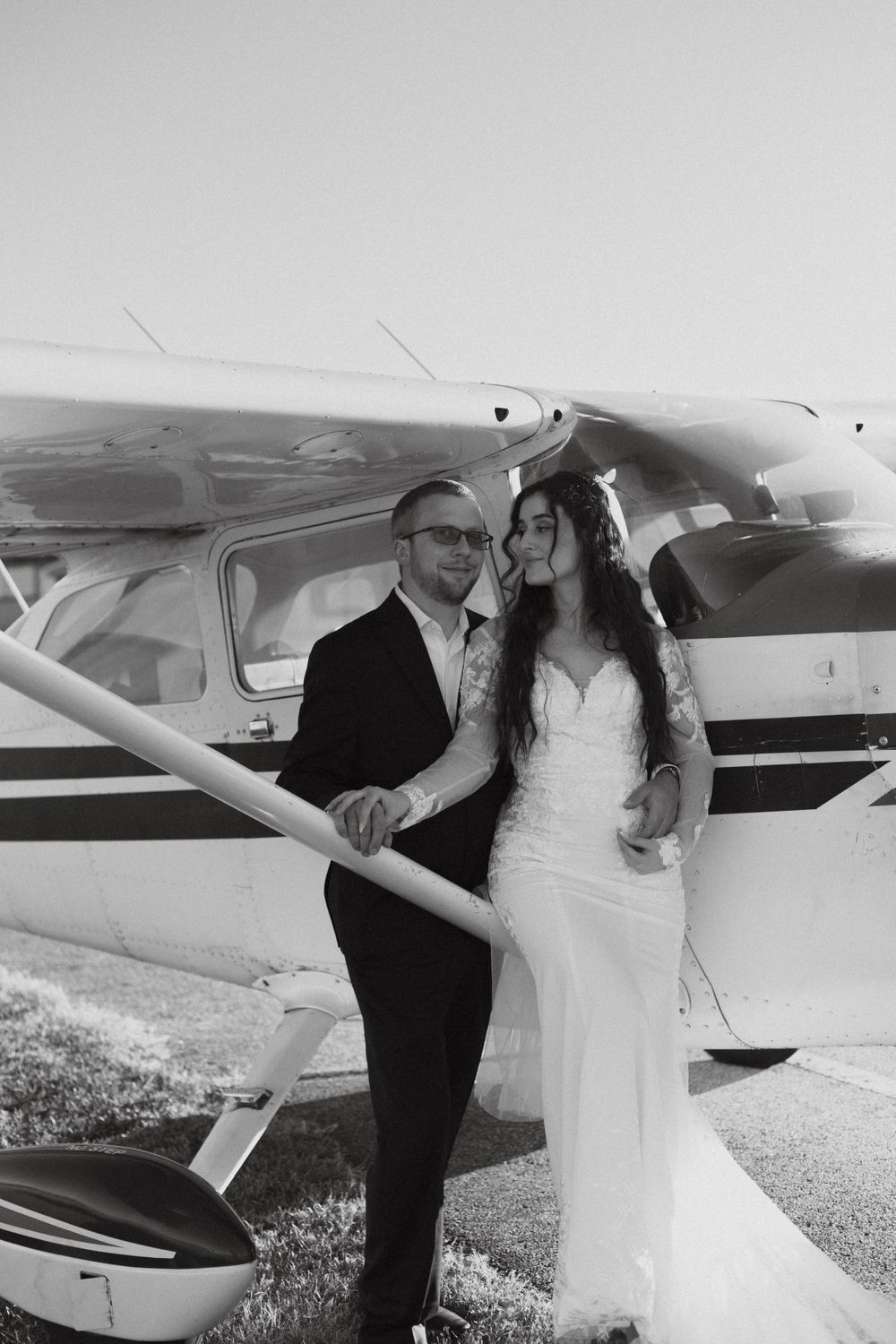 Black and white wedding portrait of couple posing by small aircraft.