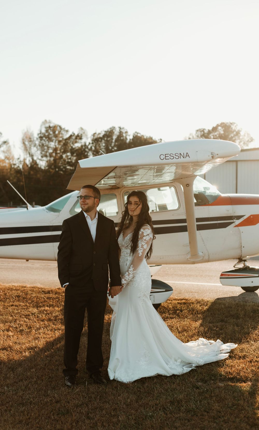 Golden hour wedding portrait of couple standing in front of Cessna airplane.