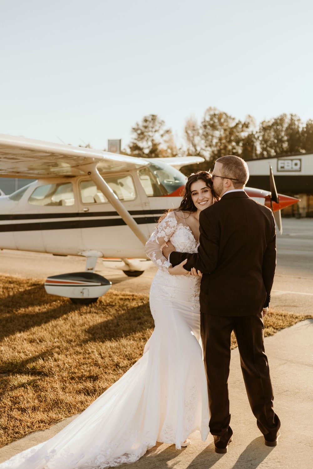 A sunset wedding photoshoot near a small aircraft on a grass airfield.
