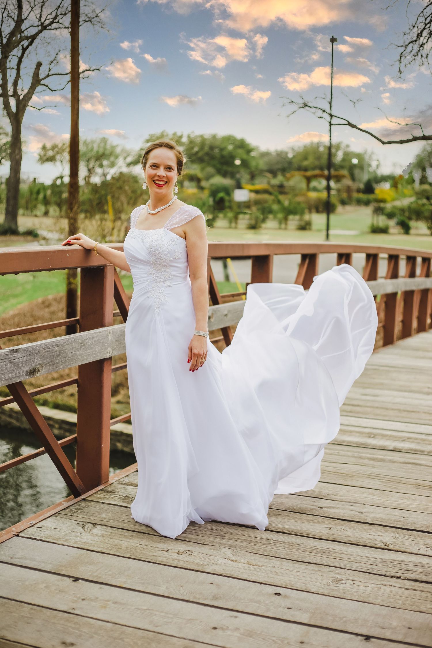 White wedding dress flows in the breeze on a wooden bridge during sunset.